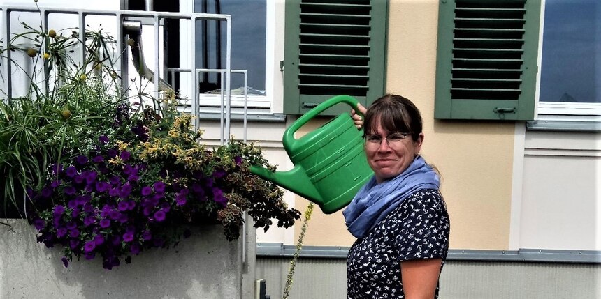 Frau mit Gießkanne neben Balkonkasten